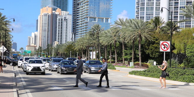 Pedestrians crossing Collins Avenue using a crosswalk.